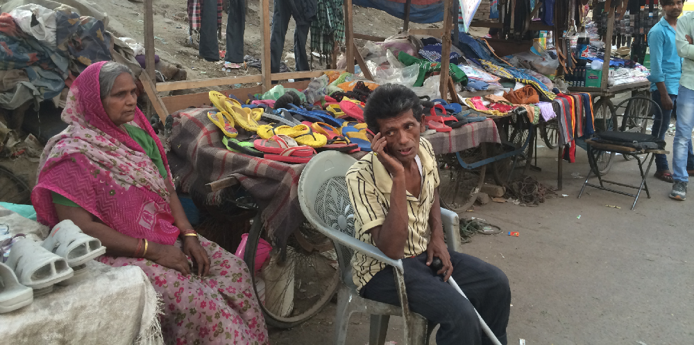 a man & woman sitting beside a footwear stall